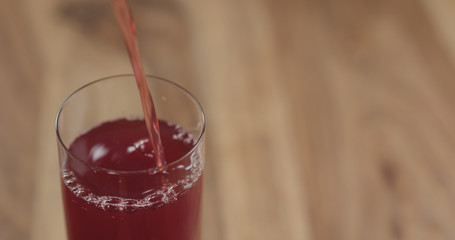 Closeup pouring cranberry juice into the glass on wood table