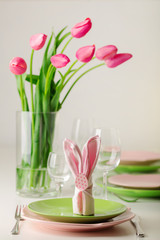 Happy easter. Decor and table setting of the Easter table is a vase with pink tulips and dishes of pink and green color.