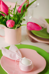 Happy easter. Decor and table setting of the Easter table is a vase with pink tulips and dishes of pink and green color.