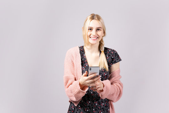 Studio shot of gorgeous young blonde woman with long straight hair wearing soft pink loose knit oversized sweater and feminine black dress. Gray isolated background, copy space, close up, portrait.