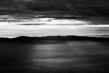 Sun rays coming down from some clouds over a valley filled by fog, illuminating part of it