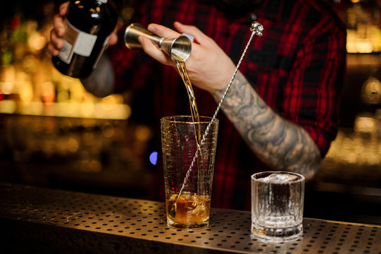Bartender pouring a drink making Rusty Nail cocktail from the steel jigger to the measuring cup