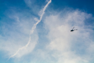 The blue sky with white clouds in the warm summer. Flight of the helicopter highly over the head.