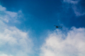 The blue sky with white clouds in the warm summer. Flight of the helicopter highly over the head.