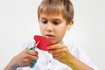 Red paper heart in kid hands. Child cutting red paper heart with scissors