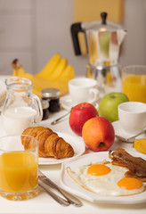 Breakfast time. Fried eggs and bacon. Croissants and orange juice, jam. Coffee with cream or milk. Fruits - bananas, red and green apples.
