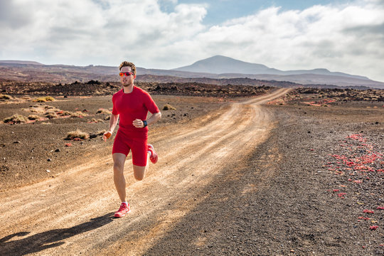 Trail running athlete fitness man runner sprinting on desert dirt road wearing compression clothes and wearable tech smartwatch watch for cardio tracking. Summer outdoor landscape.