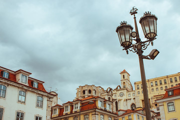 Fototapeta na wymiar Street lamp against cloudy sky and historical center of Lisbon, Portugal. Lisbon landmark. Ancient architecture in Europe. Travel concept. Traditional medieval buildings. Old street lantern and houses