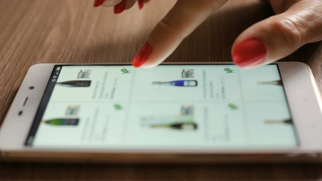 Woman orders champagne wine home in an online store. Female selects the alcohol in the grocery online store. Close-up. 4K UHD. Screen is blurred.