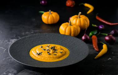 Pumpkin orange cream soup in black plate. Dark photo