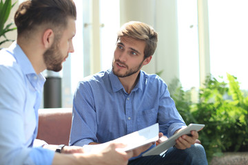 Mature businessman using a digital tablet to discuss information with a younger colleague in a modern business office.