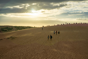 Picturesque Sunset in the Red Sand Dunes in Vietnam with Tourists sitting on top of a Dune