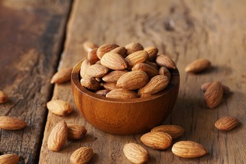 Almond nut in wooden bowl on wooden table with green leaf background