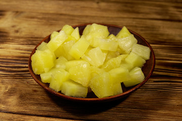 Canned pineapple pieces in ceramic plate on wooden table