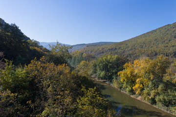 The mountains are covered with forests, and the river flows into the gorge on a clear autumn day. Beautiful landscape.