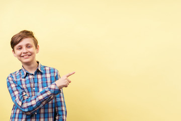 enthusiastic motivated overexcited boy points with index finger at empty space over yellow...