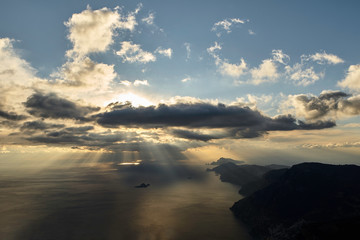 Tramonto con sole nascosto dalle nuvole ed effetto Tyndall su penisola sorrentina