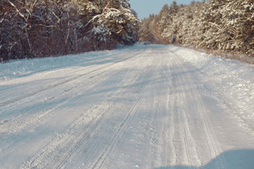Obraz premium Snow covered road surrounded by trees on a winter day.