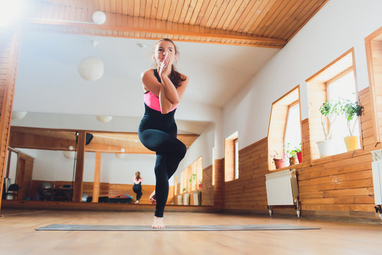 Young attractive woman practicing yoga, standing in Eagle exercise, Garudasana pose, working out, wearing sportswear, suit, indoor full length, studio background.