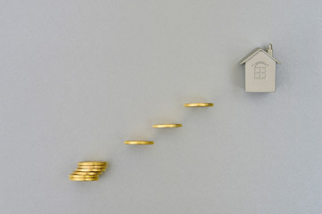 Metallic imitation of the house on a grey background with shining yellow coins.