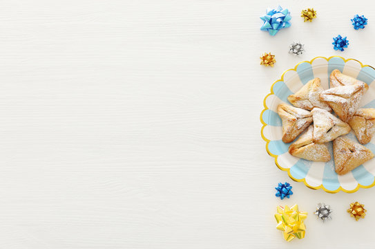 Purim celebration concept (jewish carnival holiday). Traditional hamantaschen cookie over plate and white wooden table.
