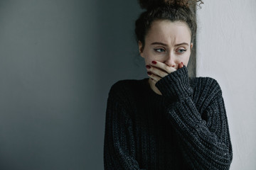 Close up of teenager with depression and bulimia sitting alone in dark room. She covers her face...