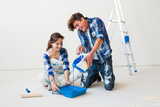 Renovation, redecoration and interiors concept - Young couple sitting on the white floor and pour paint