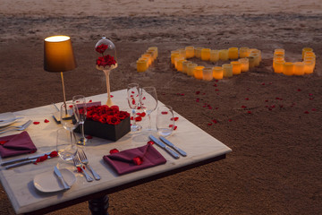Romantic beach evening dinner during sunset: candles, champagne