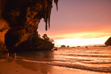 Beautiful sunset at Ao Phra Nang beach with cave and rocks on the left. The sky is pink and orange by sunset and waves are calm at white sand beach, in Ao Nang, Krabi, Thailand.