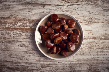 group of tasty chestnuts next to a bowl on an old wooden board
