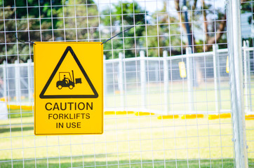 Caution sign for forklifts in use attached to the steel fence.