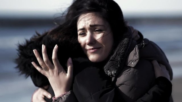 Two sister hugging and crying in front of the sea in winter from out of focus