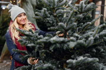 Pretty blonde girl looking for perfect Christmas tree to buy on the tree shop, outdoor. Girl using hand for check the quality, copy space - Image