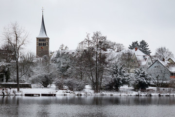 St. Martin's church near Klostersee lake, Sindelfingen, Germany. Beautiful winter landscape or cityscape with old antient church tower on horizon. Trees and buildings under snow. No people Scenic view - 243102656