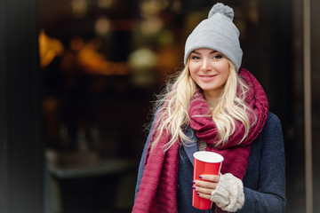 Close-up portrait of young blonde woman drinking coffe and enjoying the morning on the street. - Image