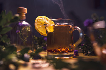 Black tea with lemon in a transparent mug, violet flowers, beautiful dark blurry background