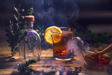 Black tea with lemon in a transparent mug, violet flowers, beautiful dark blurry background