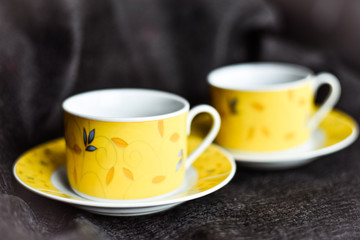 Two yellow cups of coffee on black background. Selective focus