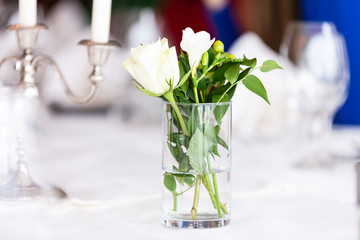 Ein Glas mit Weißer Rose steht als Schnittblume und Dekoration auf einem festlich geschmückten Tisch neben Kerzenhalter