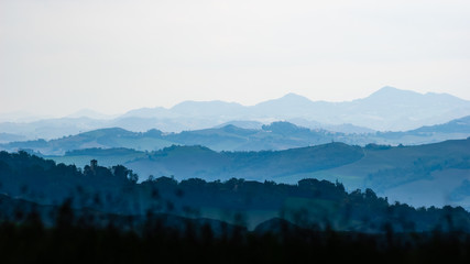 The meadows and the hills of the Montefeltro between Pesaro and Urbino, Italy, covered by trees in the shadow. The landscape disapears in the far distance haze
