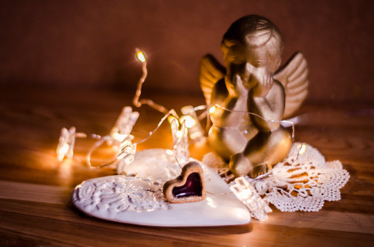 Golden figure of an angel with lights of the garland against a background of ceramic handmade hearts.