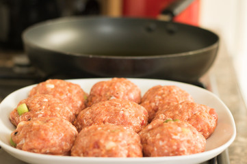 Pre-prepared fresh meat cutlets are on a plate against a background of frying pan on kitchen stove. Concept: cooking.