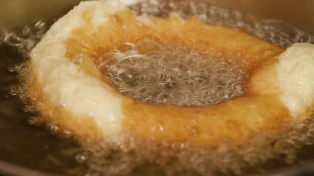 Donut fried in boiling oil. The chef turns a donut over with a skimmer, slow motion close-up view