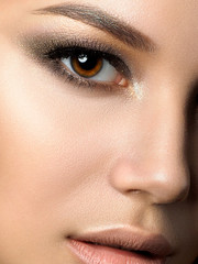 Close up beauty portrait of young woman with golden makeup. Perfect skin and fashion makeup, smokey eyes. Studio shot. Sensuality, passion and skincare concept. Extreme closeup, partial face view