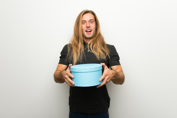 Blond man with long hair over white wall surprised because has been given a gift