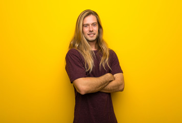 Obraz premium Blond man with long hair over yellow wall keeping the arms crossed in frontal position