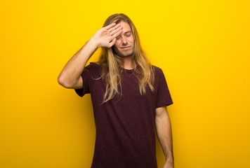 Blond man with long hair over yellow wall with tired and sick expression