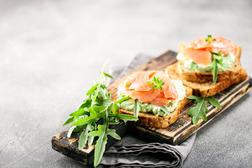 Green cream cheese, salmon and arugula sandwich on a wooden board. Smorrebrod