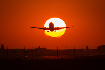 Silhouette of an air plane over the sun with beautiful red clouds in background