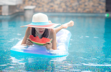 water melon holding by hand of woman floating relax on inflatable tube in swimming pool , happy holidays vacation, enjoy life confortable